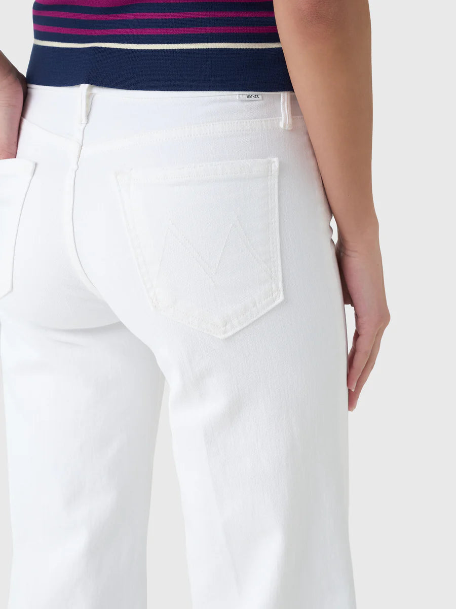 A person is shown from the waist down wearing Mother’s The Roller Fray high-waisted wide leg white jeans, paired with a navy top with pink stripes. One hand rests by their side and the jeans’ back pocket is visible.