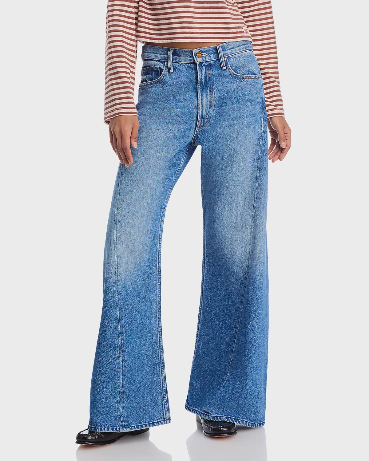 Wearing The Lemon Twist Sneak by Mother—high-rise, wide-leg blue jeans in a five-pocket style—a person stands against a plain white background, with only their lower half and a brown and white striped top visible.