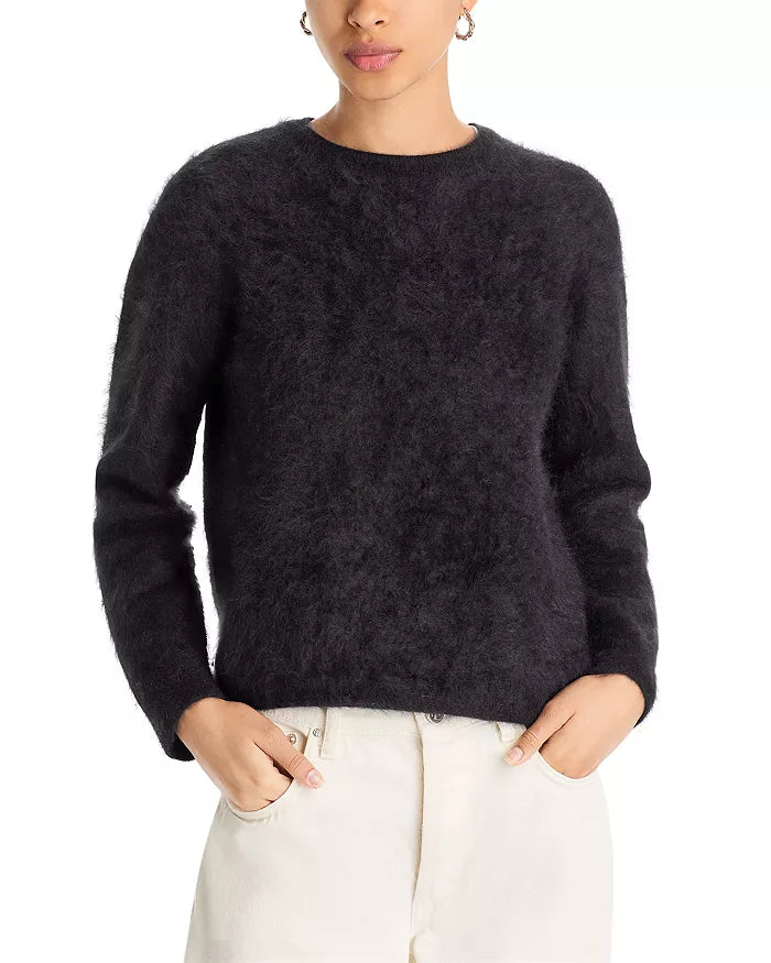 A person wearing the Jumper 1 2 3 4/CR2 Brushed Crew—a fuzzy black cashmere crew neck jumper with long sleeves—and off-white pants, stands with hands in pockets against a plain white background.