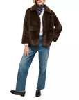 Wearing the Duane St Jacket in dark brown faux fur by Alex Mill, blue jeans, black loafers, a white shirt, and a colorful scarf, a person stands with one hand in their pocket against a white background.