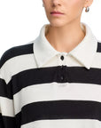 A person with short hair and hoop earrings is shown from the shoulders up, wearing the ASKK Long Sleeve Polo—a relaxed fit black and white horizontal striped shirt with a white spread collar and black buttons.