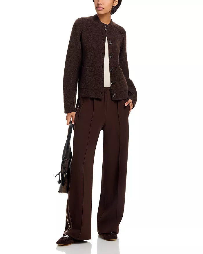 A person in the Rag & Bone bridget mock neck cardigan, wide-leg brown trousers, and brown shoes holds a black handbag while posing against a plain white background.