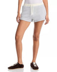A person wearing Rag & Bone’s vintage terry mix media sweatshort in light gray, paired with a white top and black sneakers with white soles, stands against a plain white background.