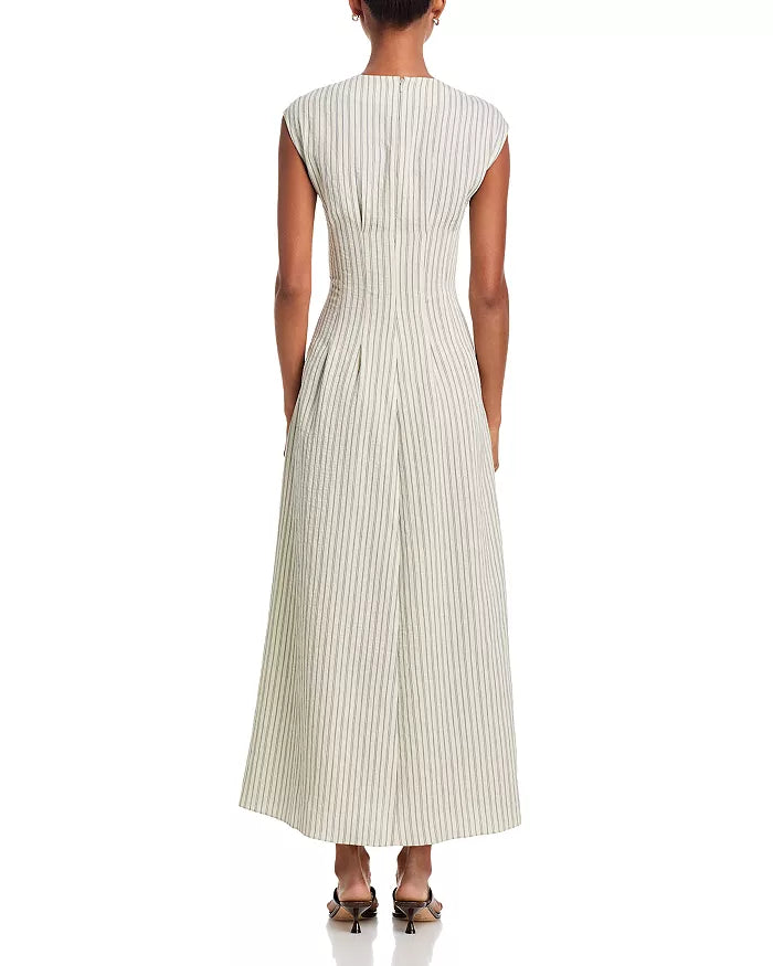 A woman faces away in the Rag & Bone ines stripe satin dress—a V-neck, sleeveless, ankle-length A-line maxi with vertical pinstripes and a fitted waist—paired with dark pointed-toe heels against a plain white backdrop.