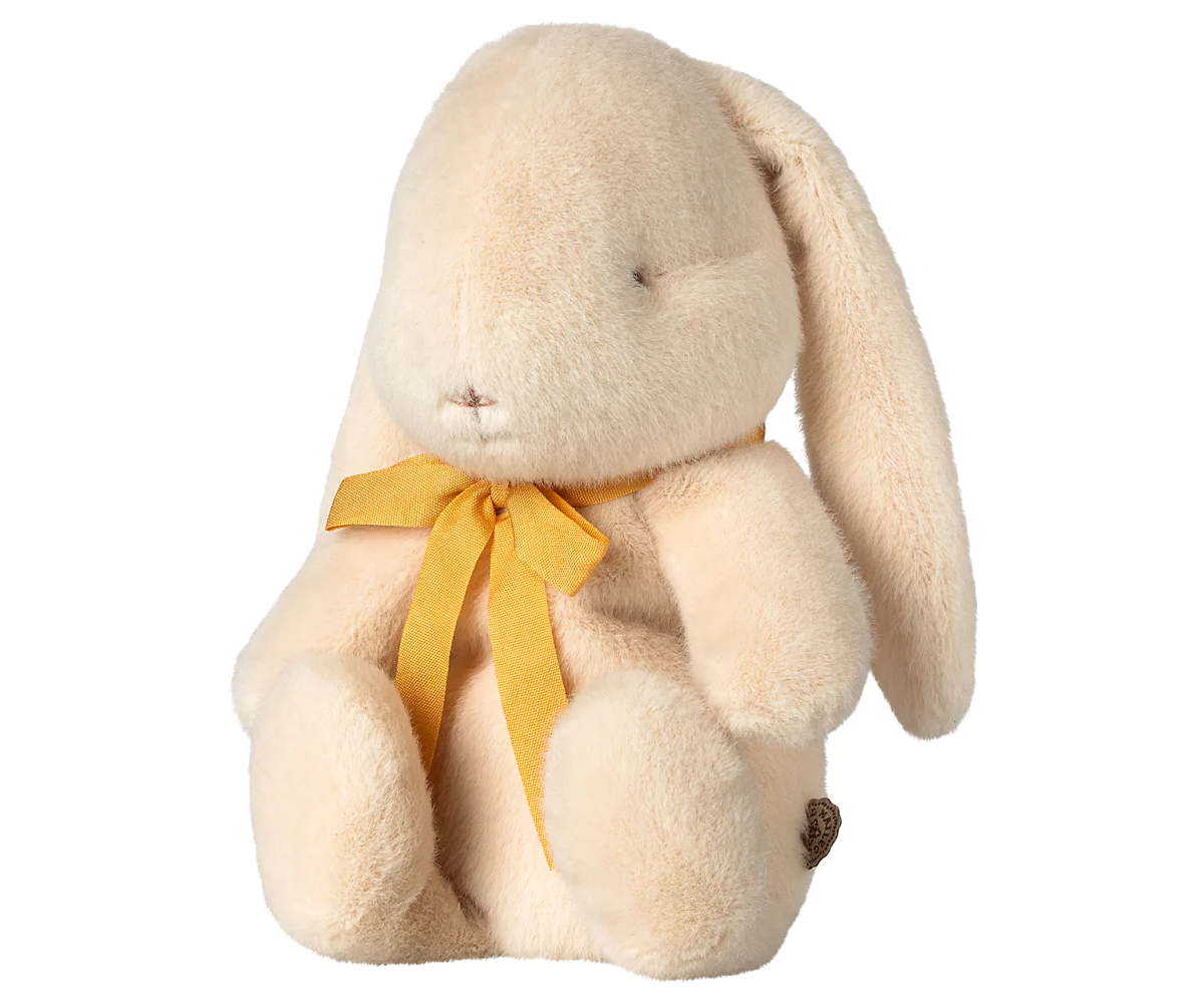 The Maileg Bunny Plush by Maileg sits upright with a floppy ear, simple stitched face, gentle fuzzy texture, and a yellow bow around its neck.