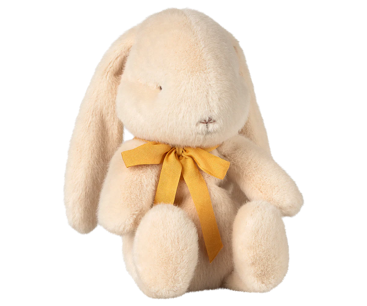 The Maileg Bunny Plush by Maileg is a cream-colored, soft plush bunny with floppy ears, simple stitched face, and a yellow ribbon bow around its neck, sitting upright against a plain white background.