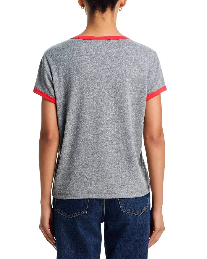 A person with their back to the camera wears Mother’s The Boxy Goodie Goodie Ringer, a gray crewneck short-sleeve t-shirt with red ringer trim on the sleeves and collar, paired with dark blue jeans.