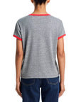 A person with their back to the camera wears Mother’s The Boxy Goodie Goodie Ringer, a gray crewneck short-sleeve t-shirt with red ringer trim on the sleeves and collar, paired with dark blue jeans.