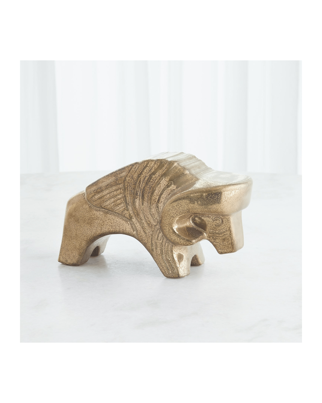 The Les Animaux-Bison-Matte Antique Gold by Global Views is a metallic bison sculpture with an abstract design. It's part of the Lemieux Et Cie collection and features textured details, showcased from the side on a smooth white surface with soft, white drapes in the background.