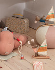Maileg stuffed animals, like mice with sailboats and the Maileg Little Sister/Beach Surfer, are playfully arranged on a wooden floor with a pastel beach ball, patterned suitcase, cans, fabric pieces, and a cat riding a hippo.