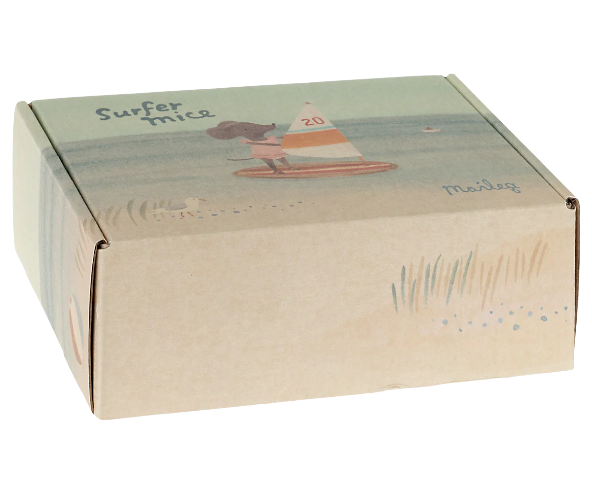 A cardboard box labeled "Maileg Little Sister /Beach Surfer" by Maileg features an illustrated mouse surfing, a grass and sandy beach scene, and suggests a toy mouse in a ruffled one piece with magnetic hands inside.