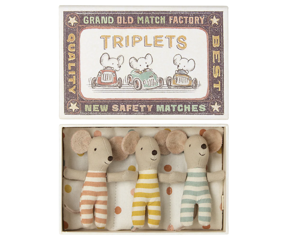 Three Maileg Mouse toys by Maileg, dressed in striped outfits, rest side by side in a small box labeled &quot;Triplets,&quot; featuring charming mouse family illustrations and a vintage matchbox-style design.