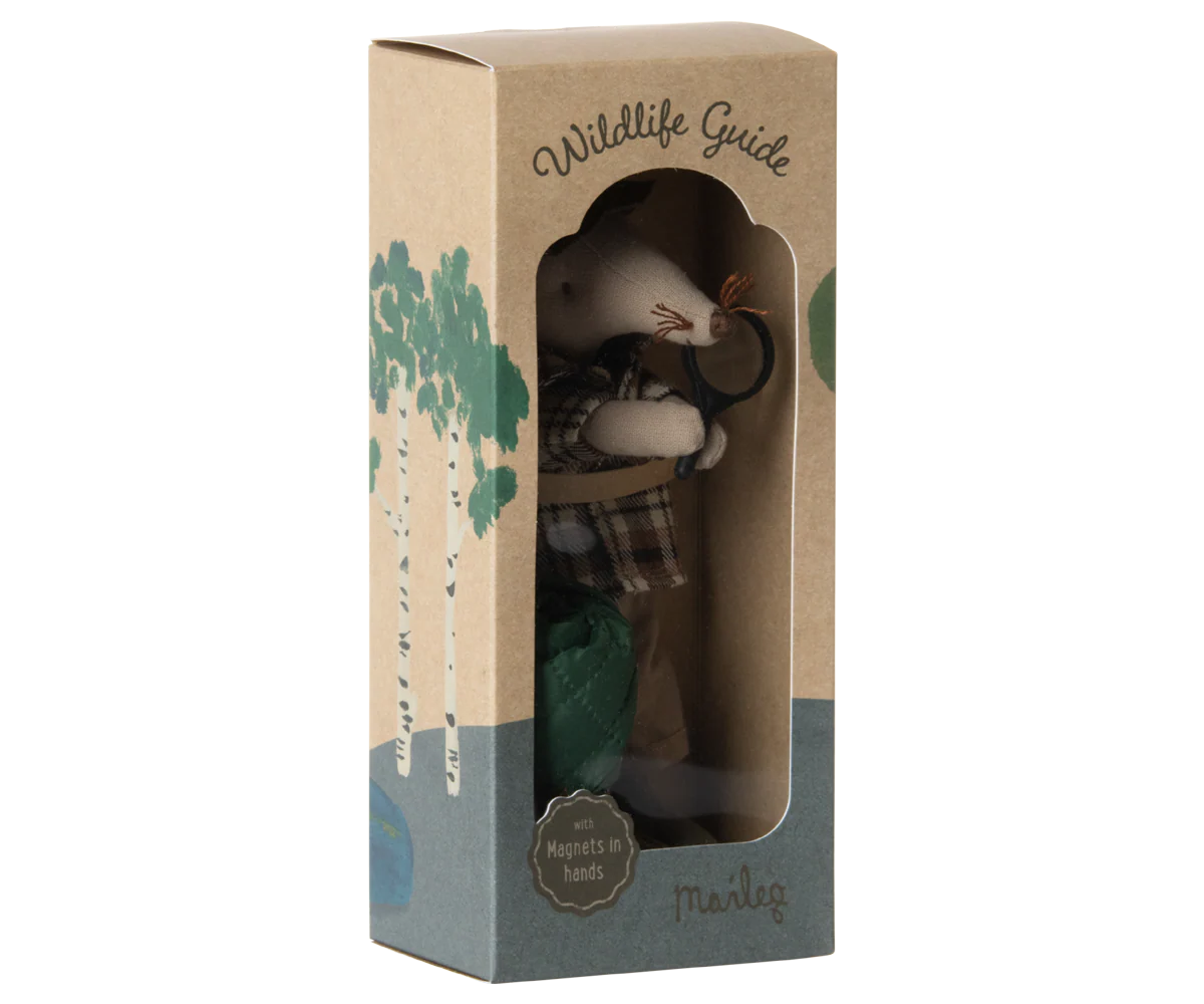 The Maileg Wildlife Guide Mouse by Maileg is a small mouse dressed in plaid for hiking, holding a stick with magnets in its hands. It comes in a cardboard box featuring tree illustrations and labeled "Wildlife Guide" and "Maileg.