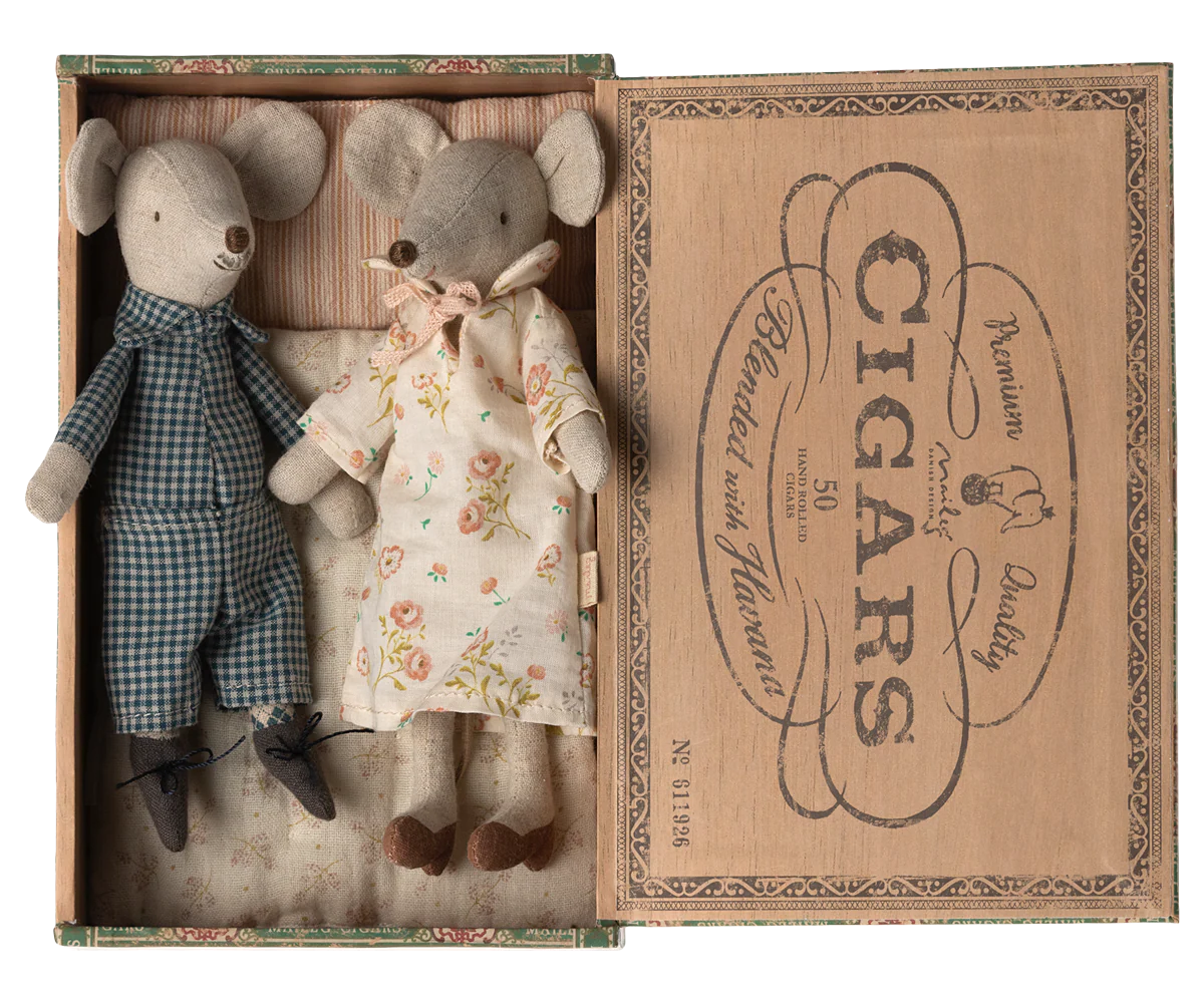 Two Maileg Mice by Maileg, one in blue checkered pajamas and one in a floral dress, rest side by side in a vintage-style cigar box with a printed label—a delightful scene from the Maileg Mouse collection.