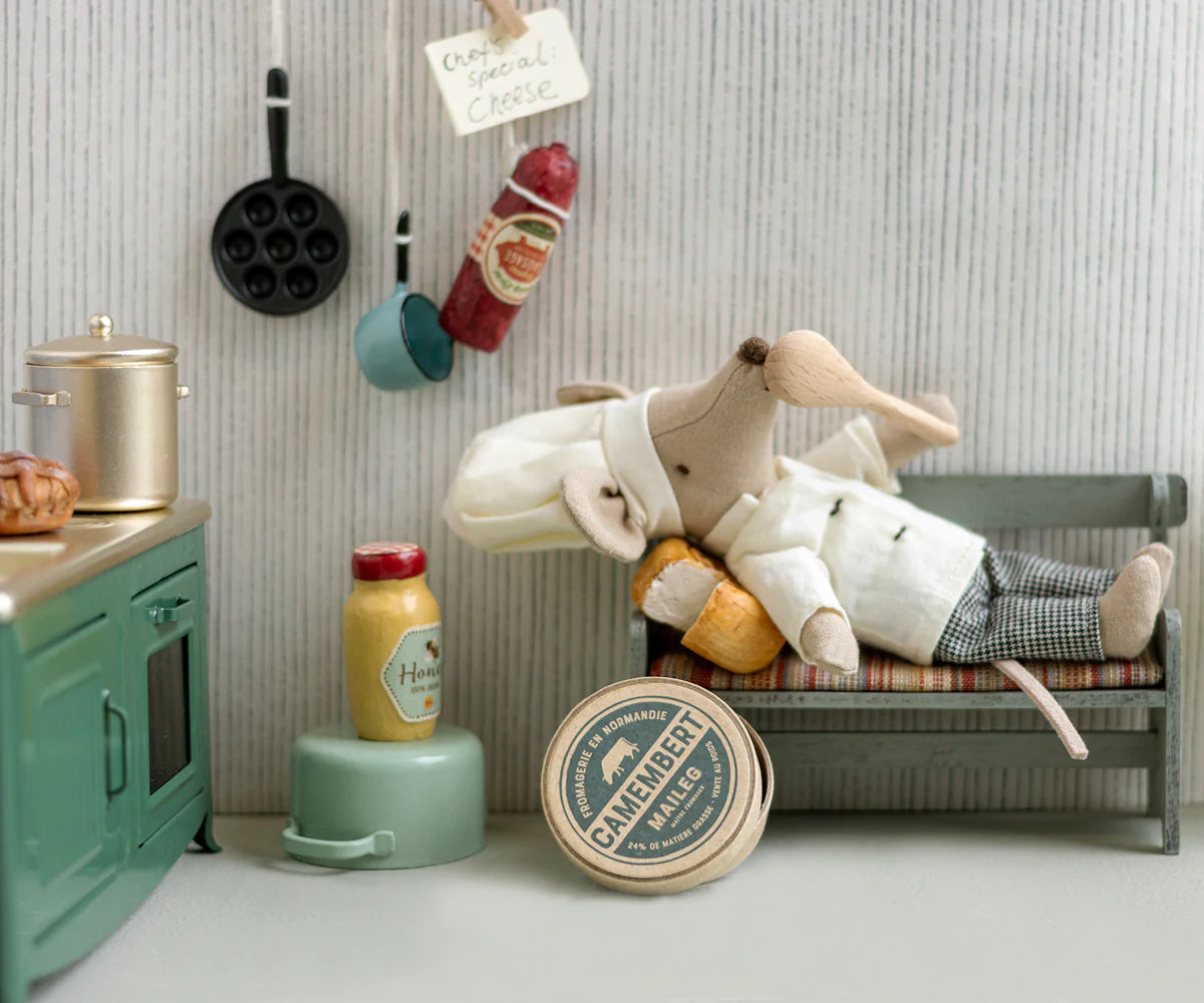 The Maileg Chef Mouse W/ Pot (Big Brother) by Maileg features a chef mouse on a bench with a baguette, plus miniature kitchen accessories like a stove, pots, mustard jar, sausage, and a Camembert box.