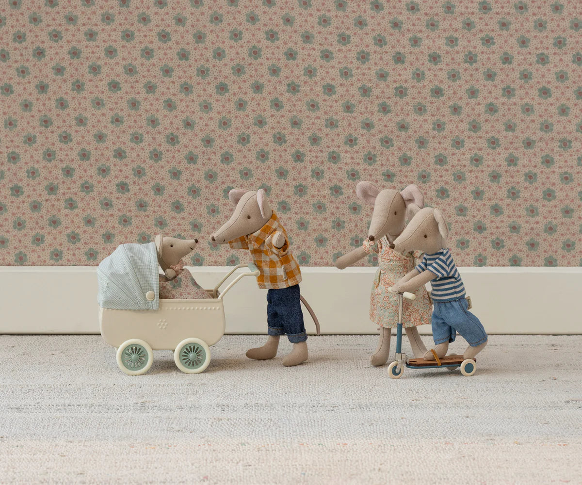 Maileg Mum Mouse, dressed in charming Maileg clothes, pushes a baby mouse in a cream pram while another mouse steers a scooter with two mice. They play on a light rug before a floral-patterned wall.
