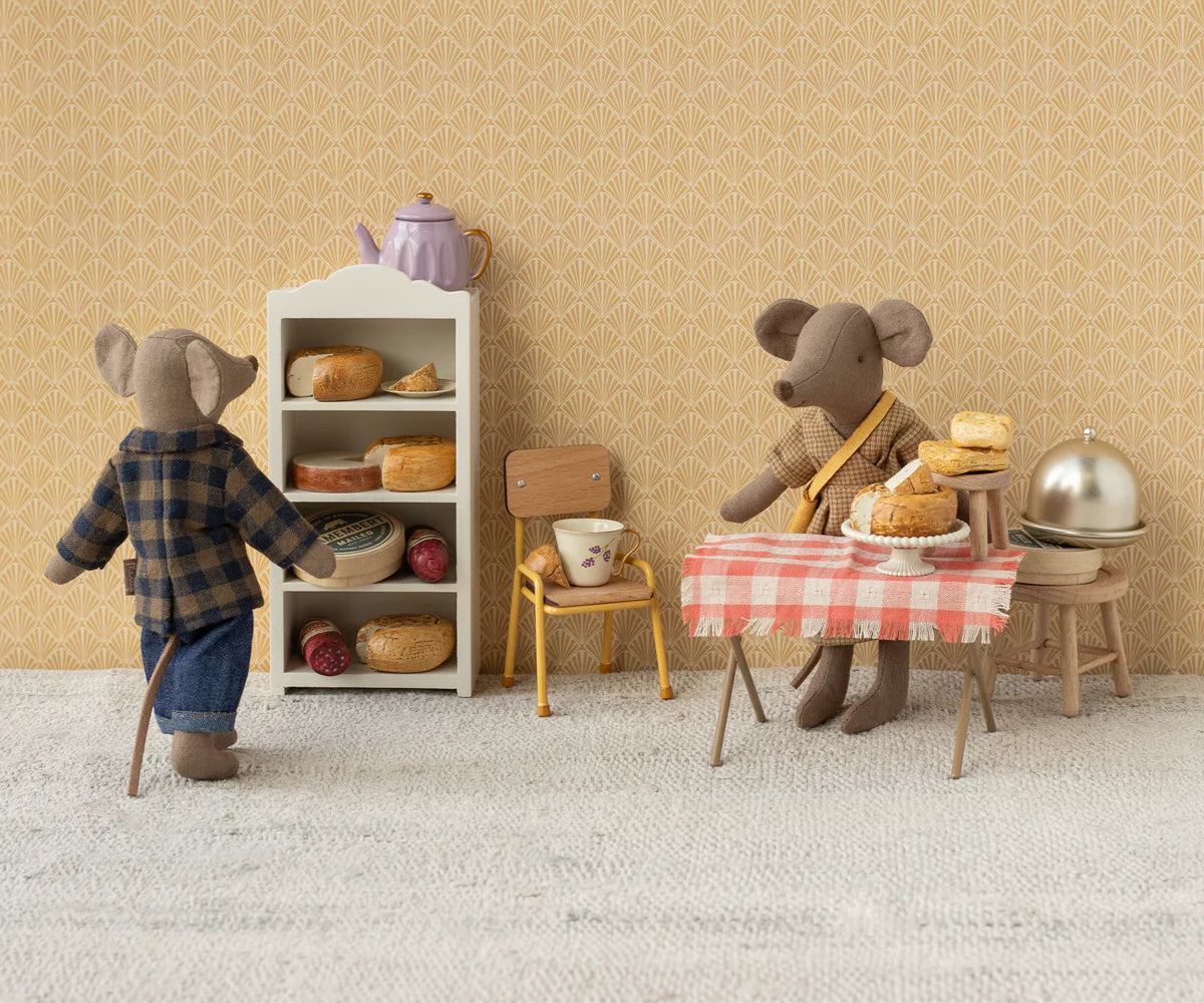 Two plush mice in a miniature kitchen: one wears the Maileg Dad Mouse Outfit by Maileg and stands near a bread shelf, while the other in a scarf sits at a table with pies, a teacup, and a red-checkered cloth.