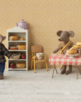 Two plush mice in a miniature kitchen: one wears the Maileg Dad Mouse Outfit by Maileg and stands near a bread shelf, while the other in a scarf sits at a table with pies, a teacup, and a red-checkered cloth.