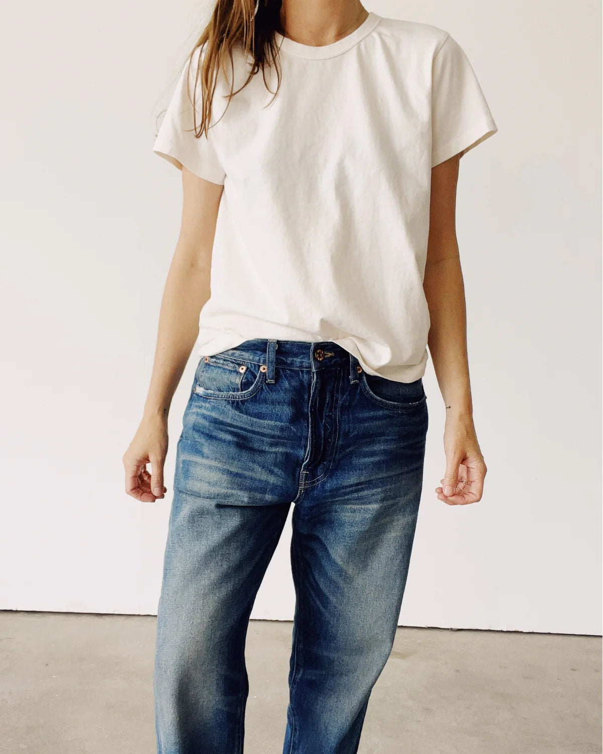 A person wearing Hey Gang’s The Crew 100% cotton plain white short-sleeve tee and blue jeans stands against a plain white wall, with their head partially out of frame.