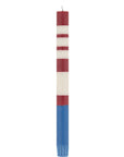 The Faire Striped Guardsman Red & Royal Blue Candles S/2 feature hand-poured red and white stripes with a solid blue base, evoking the American flag. These Fair Trade candles stand upright with unlit wicks, shown against a white background.