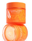 Two orange jars of Faire Tallow Body Butter Moisturizer are shown; one with the lid on, the other open to reveal creamy balm inside. Both display bold yellow text on their labels.