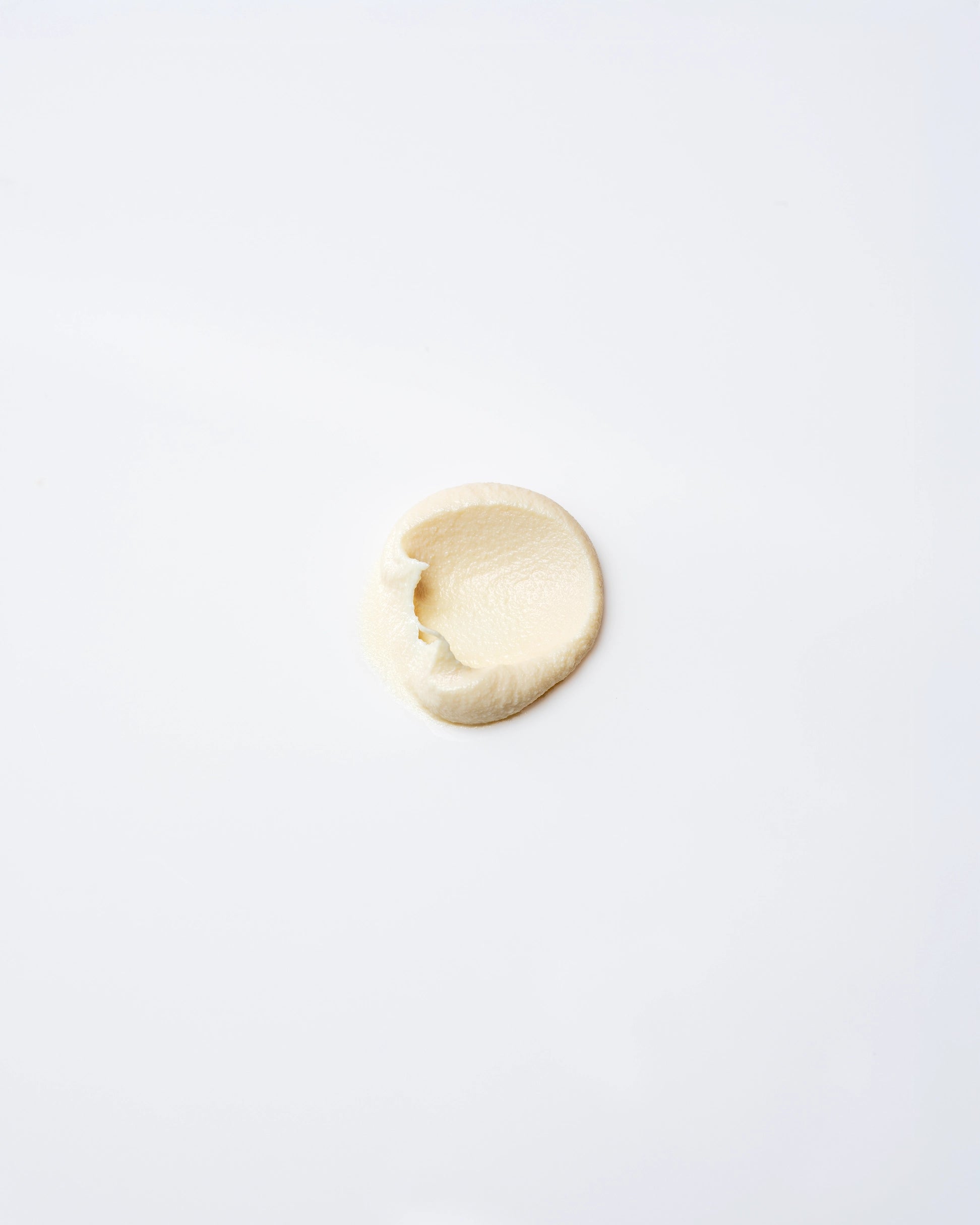 A small dollop of Faire Tallow Sunscreen SPF 50 is spread in an oval shape on a smooth, white surface.