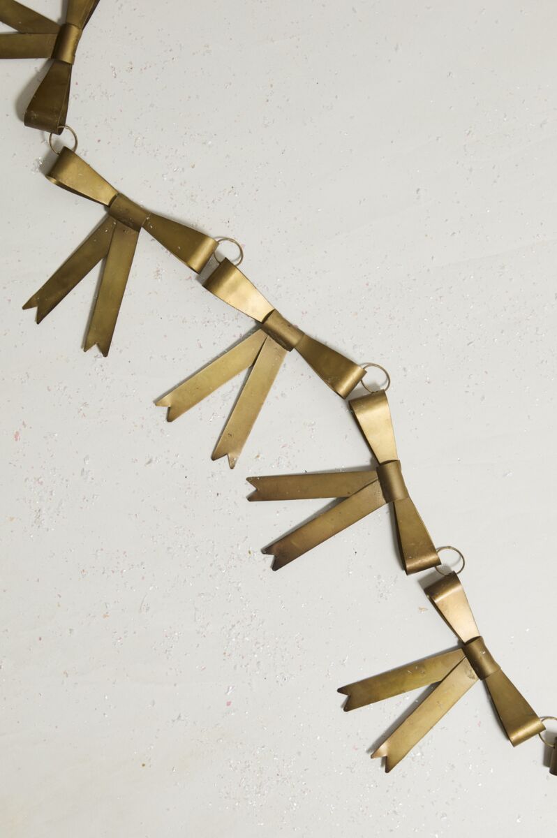 The Collectors Garland -Bow by Accent Decor features gold-colored bows linked by small rings, arranged diagonally on a light surface—making it a perfect unique holiday decoration.