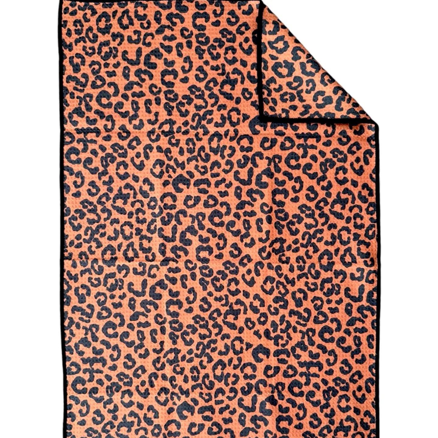 The Faire Double Sided Hand Towel features a rectangular waffle weave microfiber design with orange and black leopard print on both sides. One corner is folded to show the reversible pattern—an eco-friendly holiday choice.