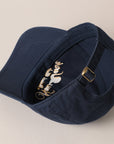 The New York Social Club Baseball Cap by Faire is displayed in navy blue with gold text embroidery. Turned sideways, it highlights an adjustable strap with a brass buckle against a beige background.