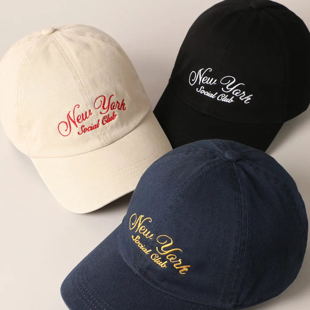 Three Faire "New York Social Club" baseball caps with text embroidery are arranged in a triangle. They come in beige, black, and navy blue, featuring the club's name in red, white, and gold letters. Each cap has an adjustable strap for a perfect fit.