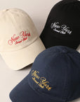 Three Faire "New York Social Club" baseball caps with text embroidery are arranged in a triangle. They come in beige, black, and navy blue, featuring the club's name in red, white, and gold letters. Each cap has an adjustable strap for a perfect fit.