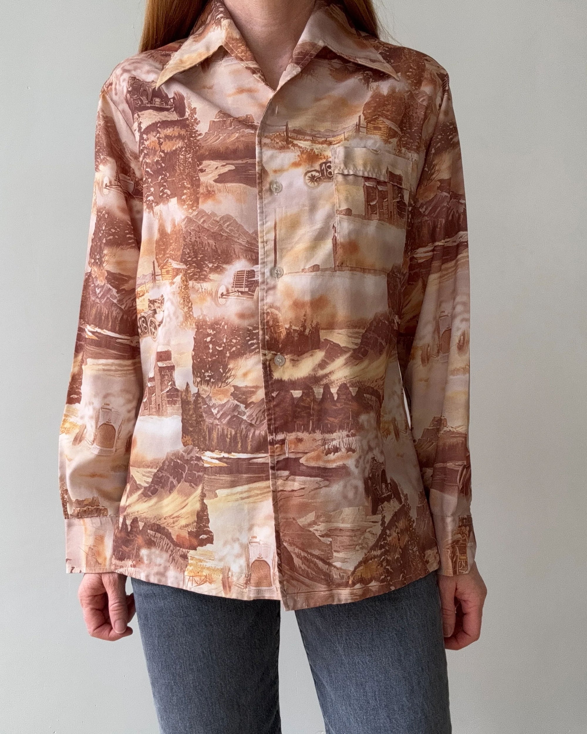A person in a medium fit, long-sleeve 1970s Silky Racer shirt by Red Vintage Co., featuring brown and beige landscape print with collar and cuff details, paired with gray pants, stands against a plain light background.