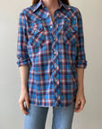 Wearing a medium, ultra-light 1970s Plaid Western shirt by Red Vintage Co.—blue and red plaid with rolled-up long sleeves, two front pockets, and white buttons—paired with light blue jeans against a plain background.