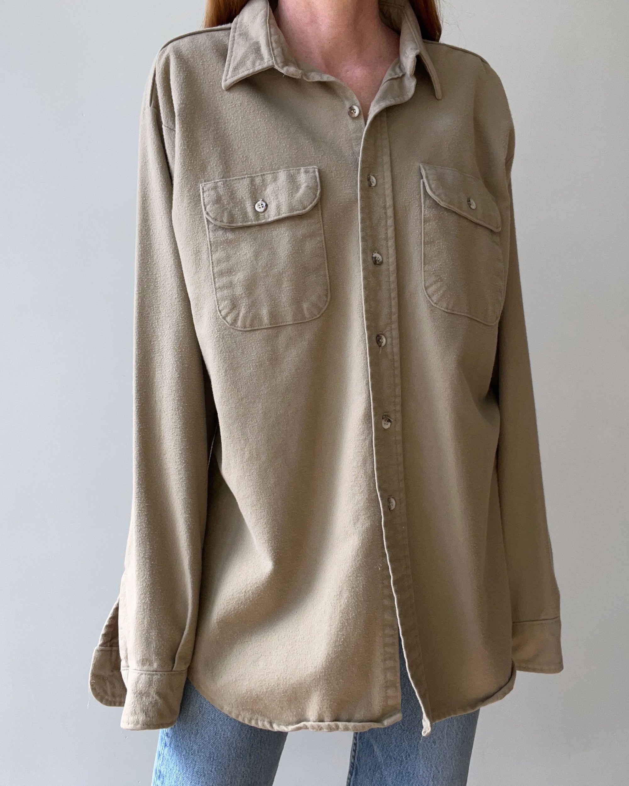 A person wears the Red Vintage Co. 1980s Tan Flannel, a loose-fitting flannel shirt with two chest pockets, paired with light blue jeans, standing against a plain light-colored background.