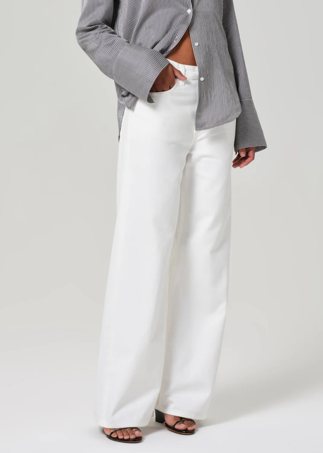 A person in a gray striped shirt with wide sleeves and Palma Straight Soft White pants by Citizens Of Humanity/AGOLDE, made from a recycled cotton blend, stands in a neutral pose without their face visible.