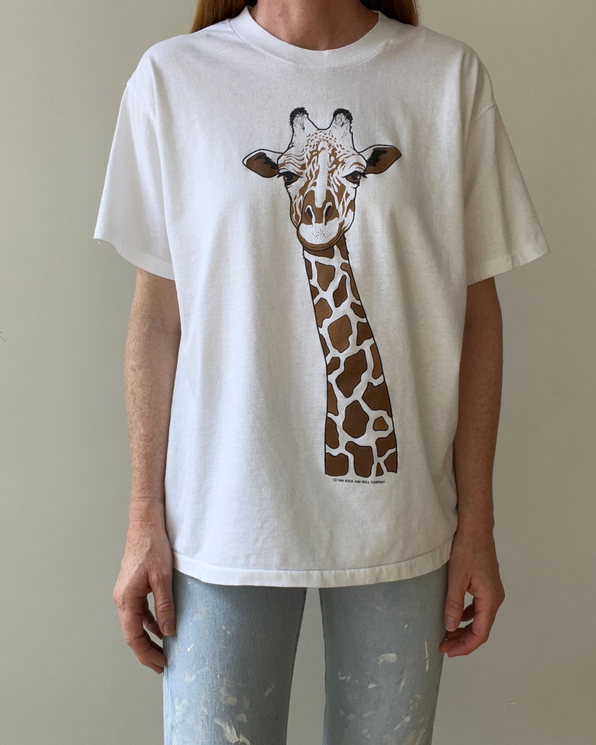 Wearing the Red Vintage Co. 1989 Giraffe Tee, a loose boxy white shirt with a bold giraffe graphic and single stitch detail, paired with light blue jeans featuring white paint splatters.