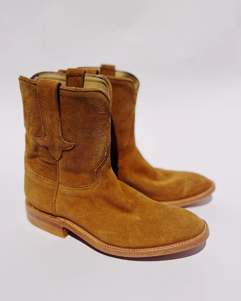 Hey Gang&#39;s The Ranch Boot showcases brown calfskin suede with decorative side stitching, a light wooden sole, and stacked heel. Placed on a plain white background, they exude timeless western charm.