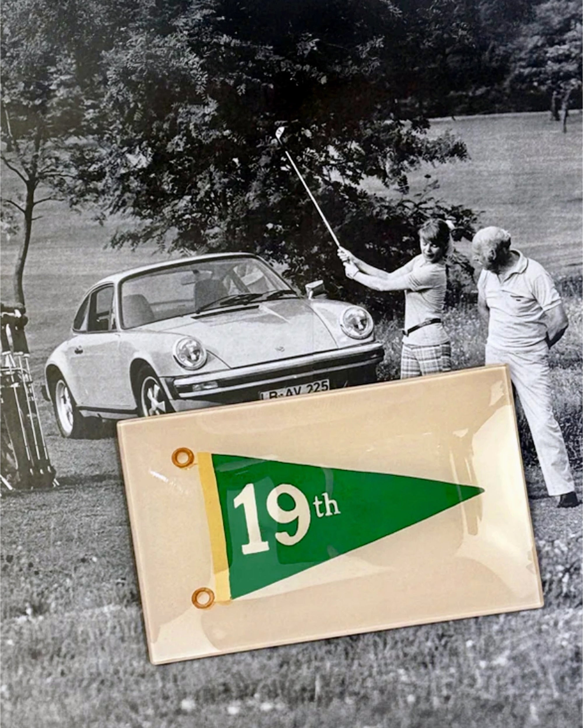 The Faire 19th Hole Glass Tray features a black-and-white photo of two golfers by a classic Porsche and a green-and-yellow "19th" pennant—ideal golf decor for any clubhouse.