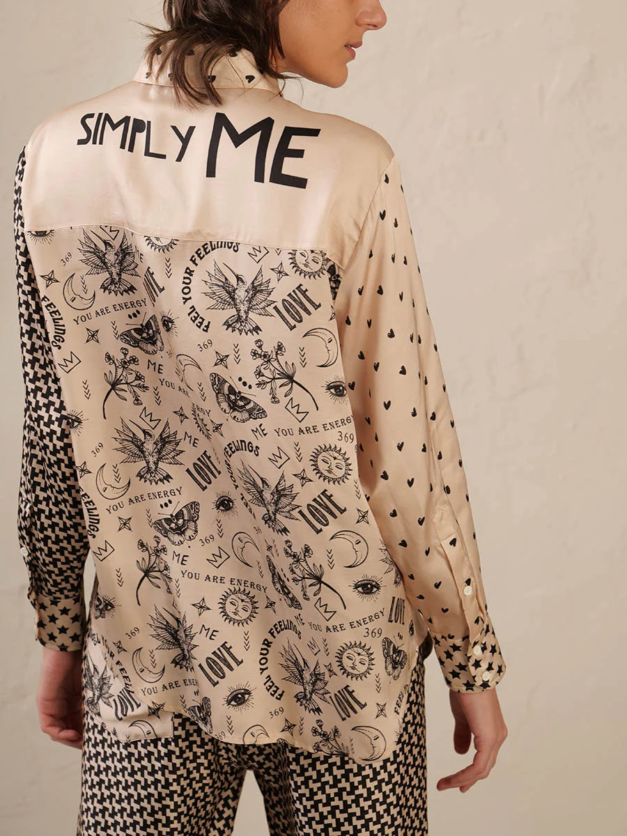 A person with shoulder-length hair is seen from behind, wearing the Me369 Scarlett Print Shirt—a 100% Viscose mixed print top with “SIMPLY ME” on the upper back—styled with houndstooth pants.