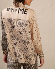 A person with shoulder-length hair is seen from behind, wearing the Me369 Scarlett Print Shirt—a 100% Viscose mixed print top with “SIMPLY ME” on the upper back—styled with houndstooth pants.