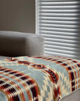 A light gray sofa is draped with the Faire Secoya Throw, crafted by an Ecuadorian artisan. Soft natural light filters through white blinds in the background.