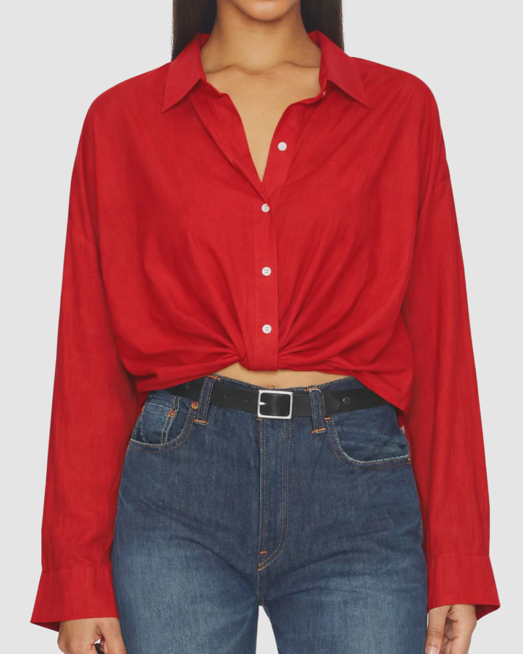 A person wears Denimist's SLIM TWISTED FRONT BEACH SHIRT in red, styled with blue high-waisted jeans and a black belt. The cropped image highlights the shirt’s twisted front and frames the shoulders and hips.