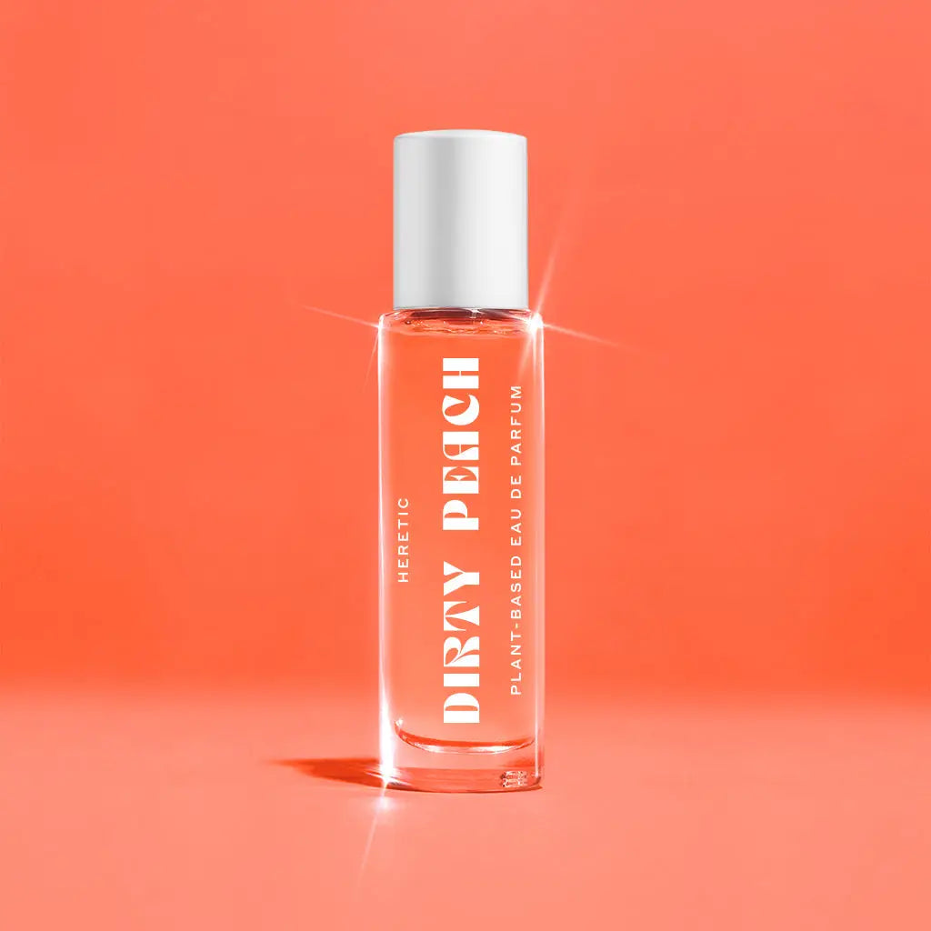 A clear glass bottle of Faire Heretic 15ML Perfume with a white cap and bold white text stands upright on a peach-colored background, evoking sandalwood and vanilla notes.