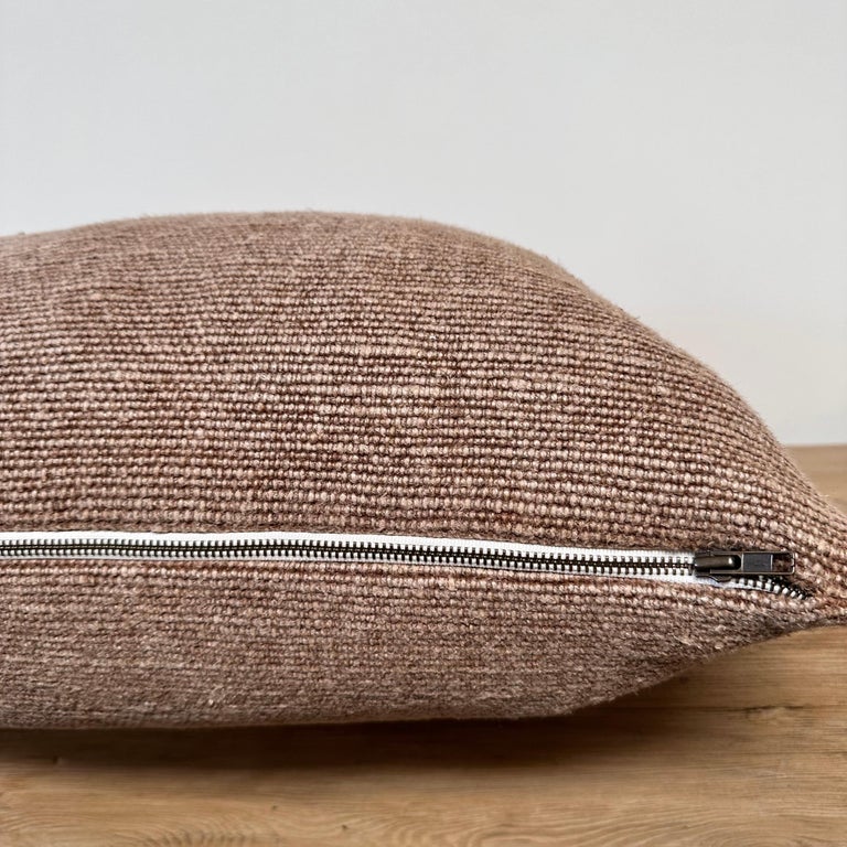 A close-up of the Faire Alora Woven Linen Havana pillow, featuring a visible silver zipper and plush down feather insert, shown on a wooden surface with a plain white background.