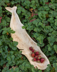 The Be Home Kiln Mango Wood Whale Dish, filled with strawberries, rests atop lush green strawberry plants dotted with ripe red berries.