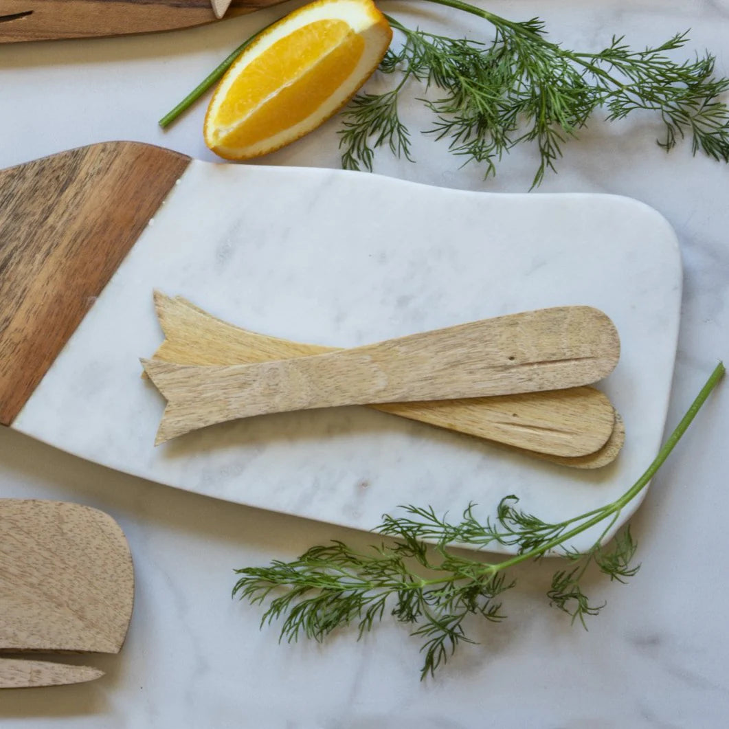 A set of Be Home Sydney Whale Spreaders rests on a marble and wood board, accented with fresh dill and an orange wedge—an elegant presentation highlighting sustainably sourced mango wood products.