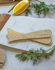 A set of Be Home Sydney Whale Spreaders rests on a marble and wood board, accented with fresh dill and an orange wedge—an elegant presentation highlighting sustainably sourced mango wood products.