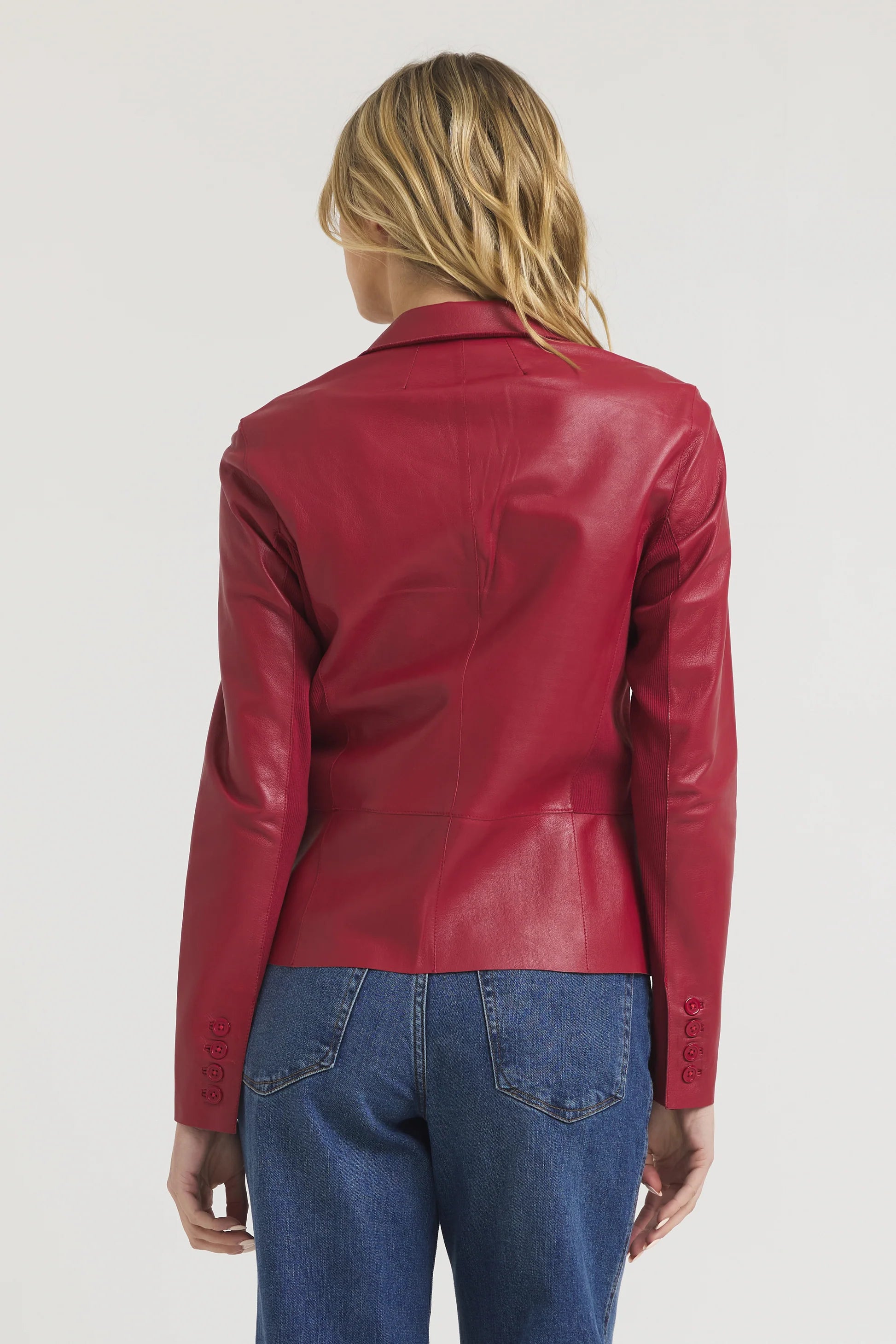 A person with long blonde hair is shown from the back, wearing the JAKETT Allison Burnished Leather jacket with blue jeans against a plain white background.