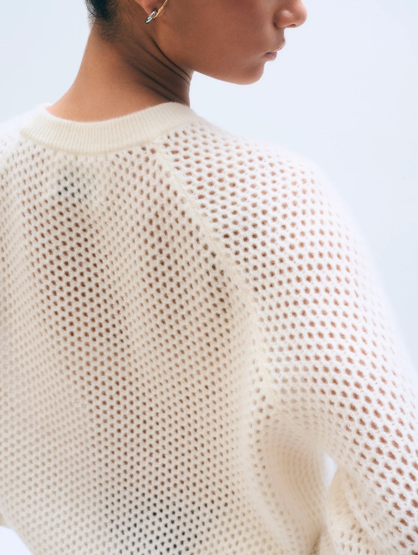 A close-up of a person wearing the White + Warren Cashmere Mesh Sweatshirt in white, highlighting the textured mesh knit on the back and shoulder. The model has short hair and a small hoop earring.