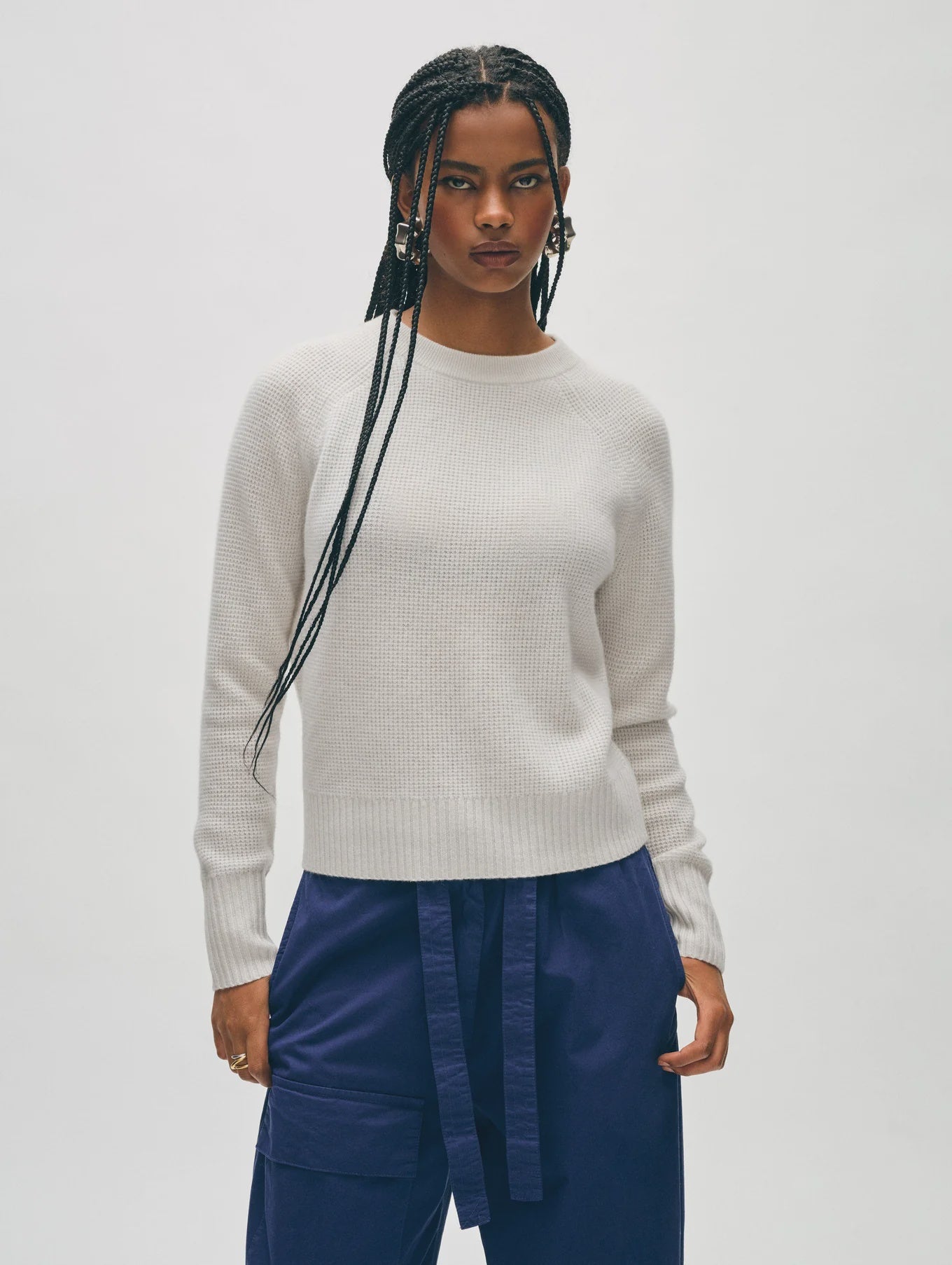 A person with long braided hair wears the Cashmere Waffle Sweatshirt from White + Warren, paired with navy blue pants. They stand against a plain background with a neutral expression, showcasing a relaxed fit.